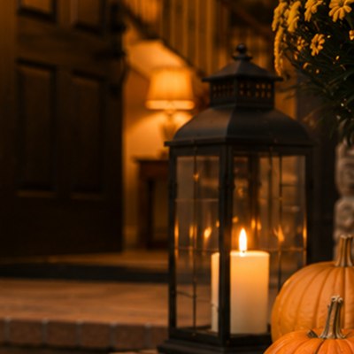 A black lantern with a lit candle glowing at dusk